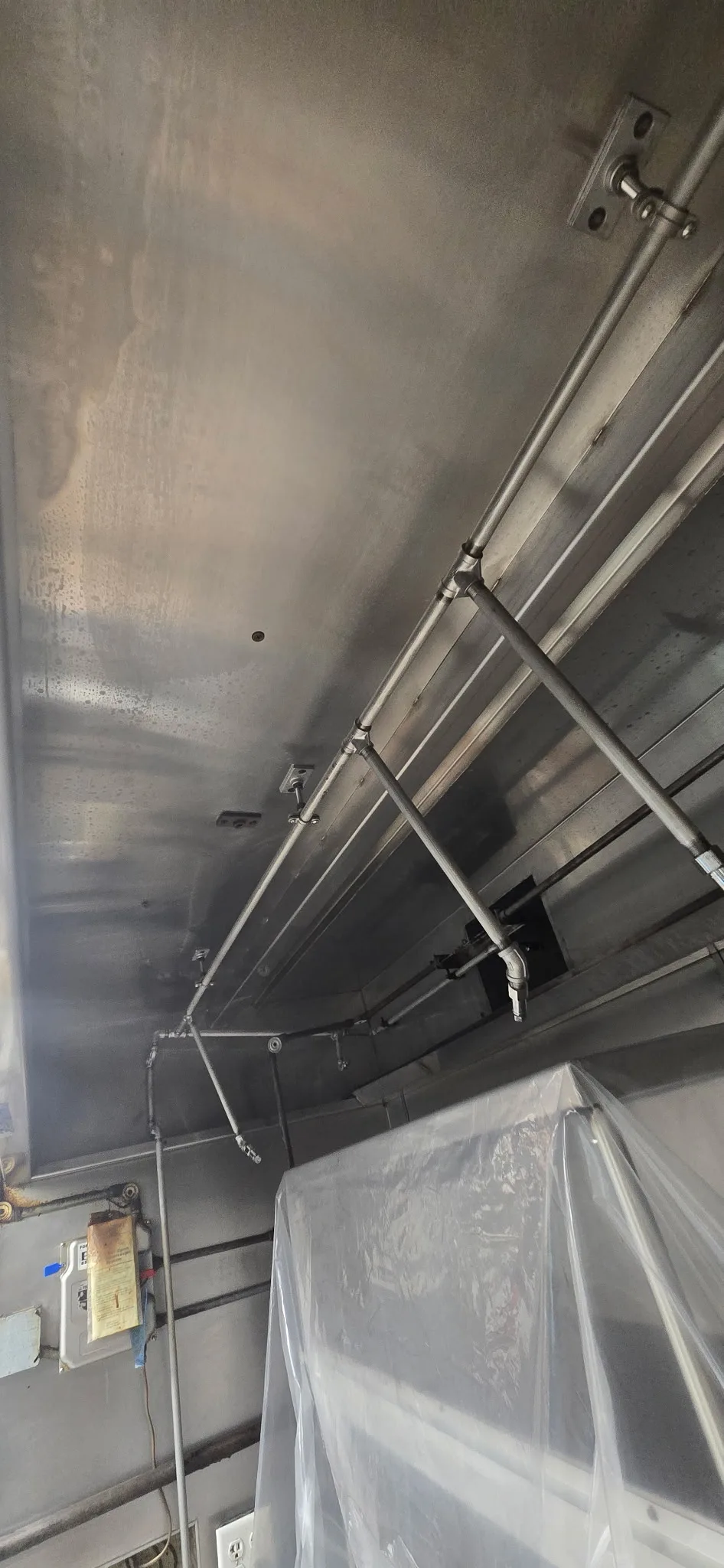 Hood interior after cleaning — full length view showing clean stainless steel plenum and polished suppression system pipes