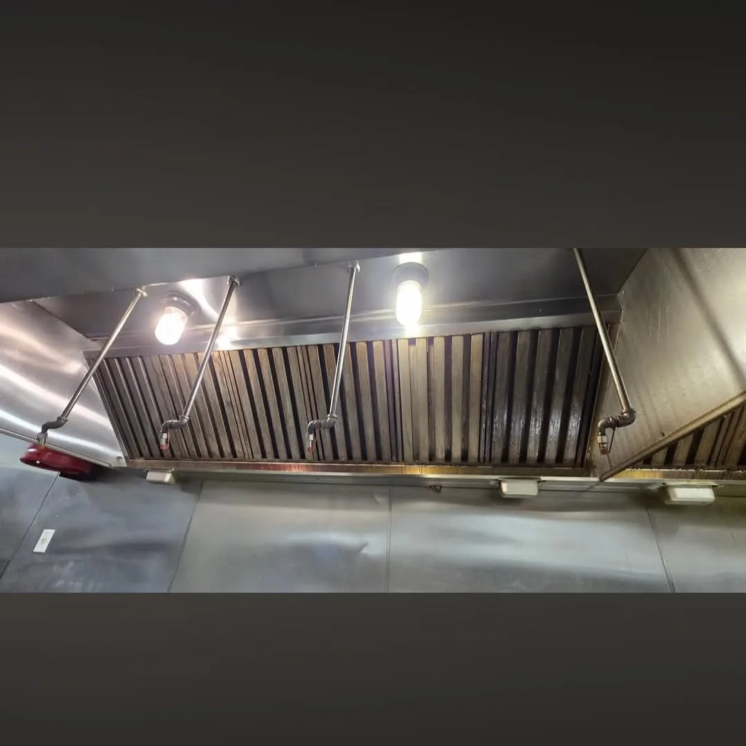 Wide commercial hood with baffle filters darkened by grease buildup before cleaning
