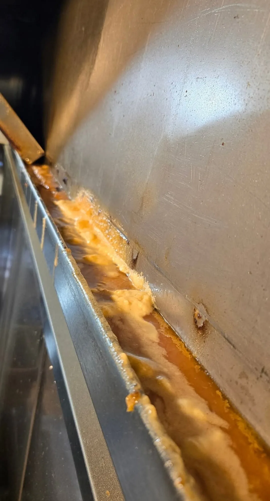 Hood drip channel before cleaning packed with orange grease buildup along the trough