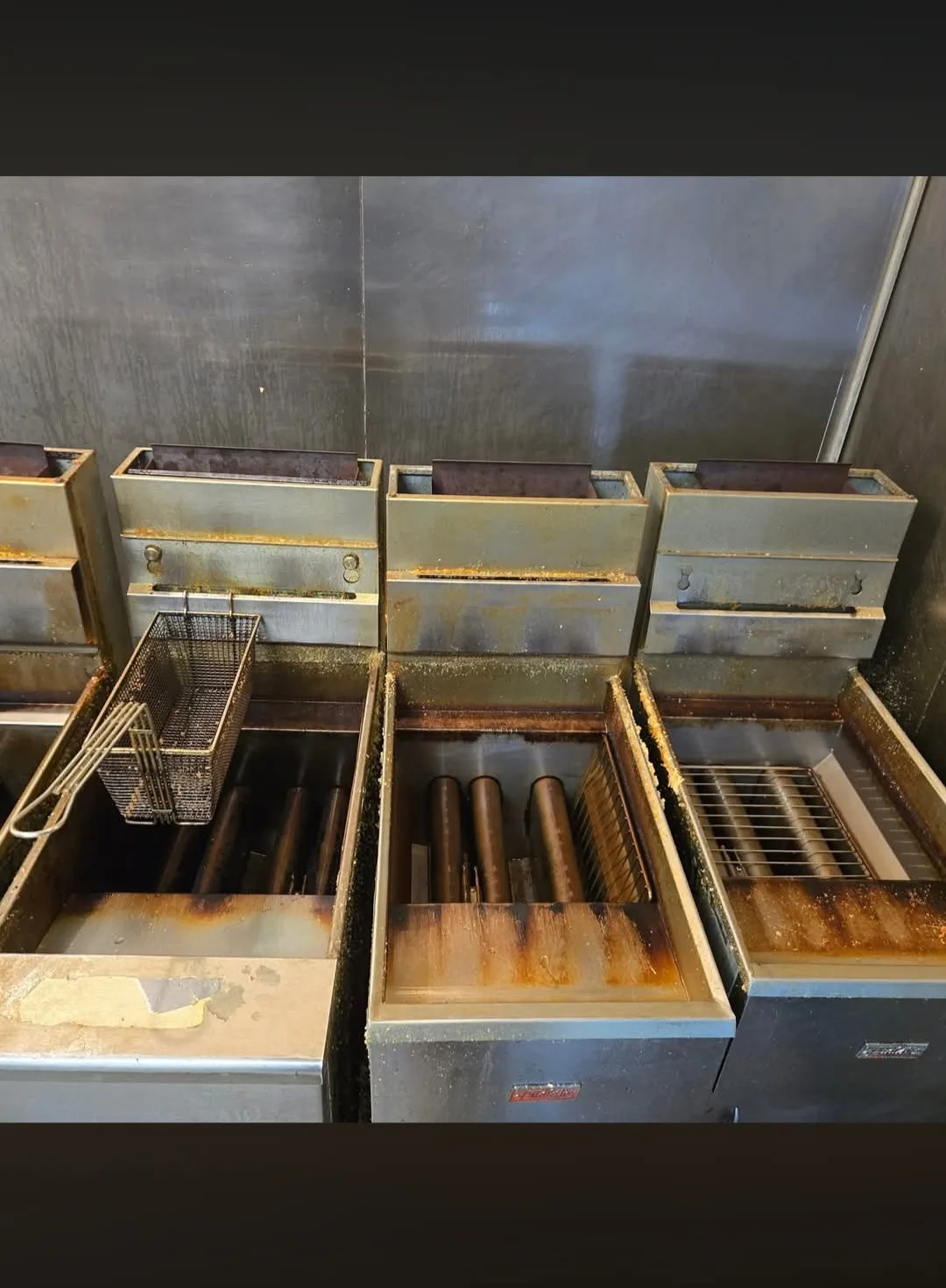 Commercial fryer vats before cleaning coated in heavy oil residue and carbon deposits