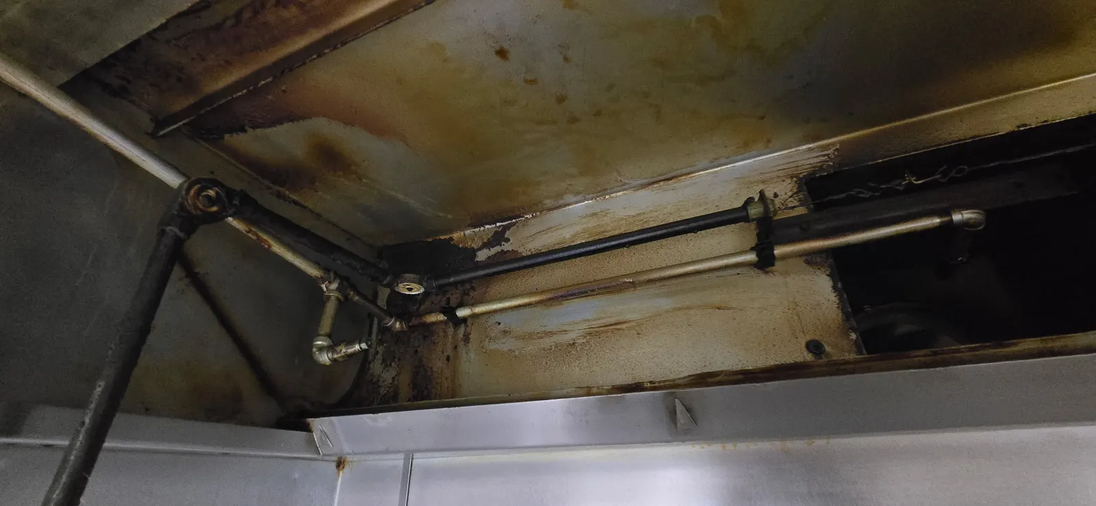 Hood interior before cleaning — wide angle showing brown grease coating every surface including suppression system pipes