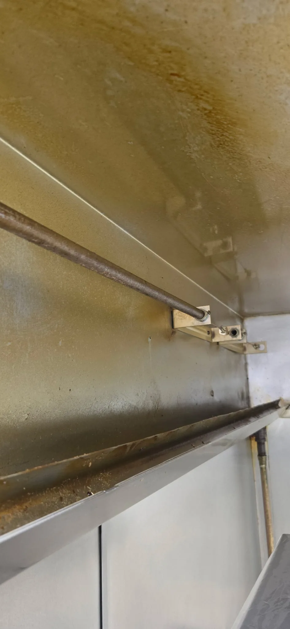 Hood interior before cleaning — corner angle showing grease buildup on plenum ceiling and suppression lines