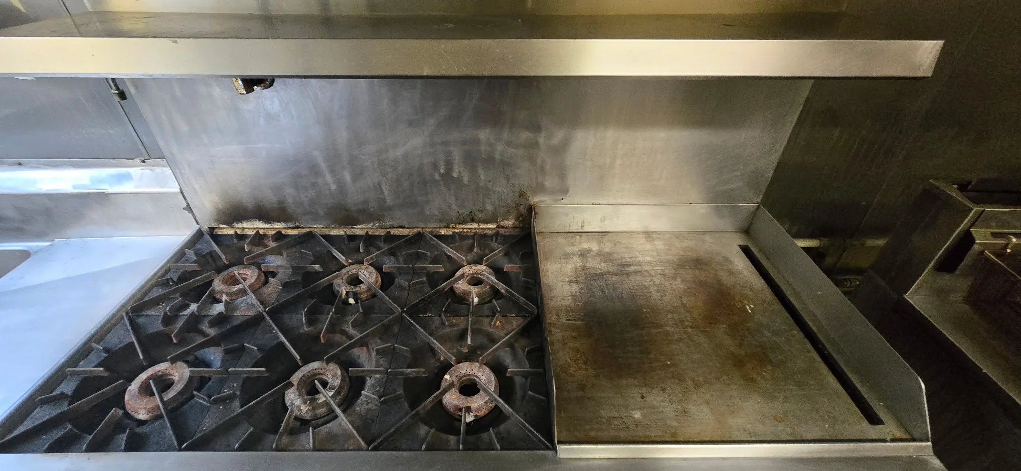 Commercial range before cleaning showing grease and carbon buildup on burners and griddle