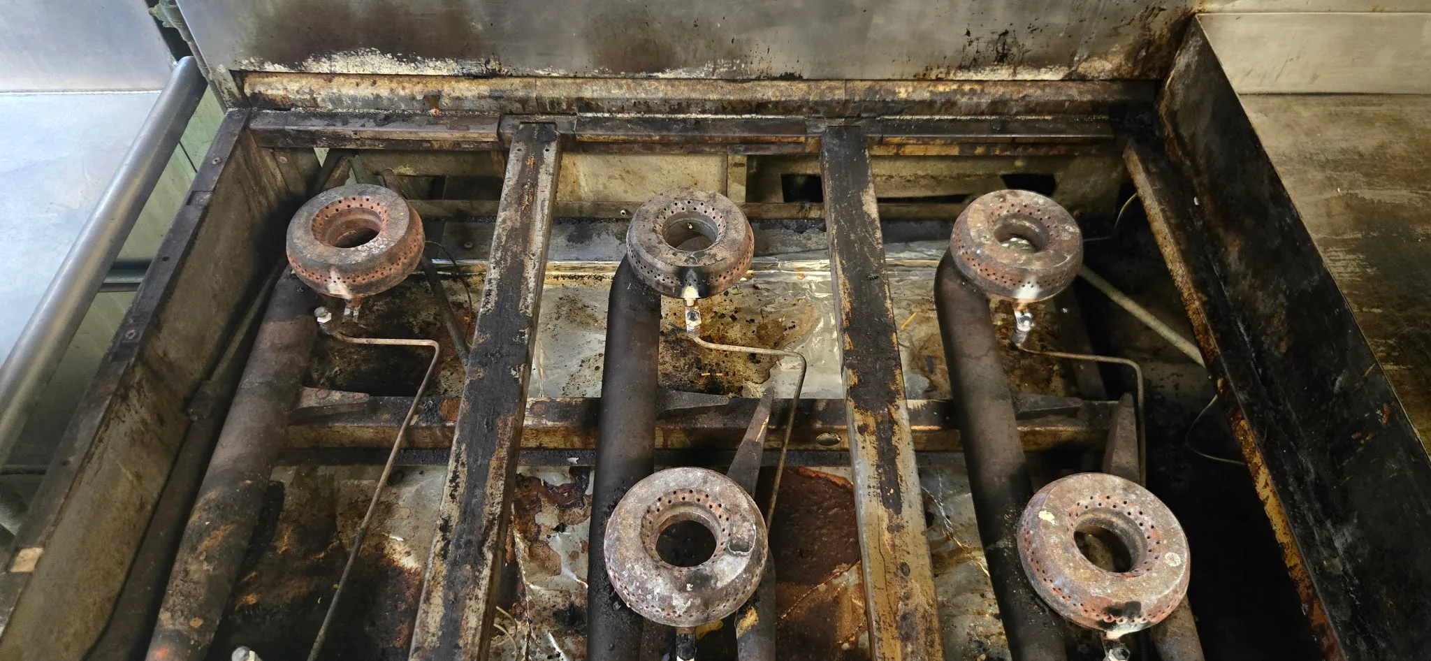 Commercial range burner heads removed showing heavy grease and carbon buildup