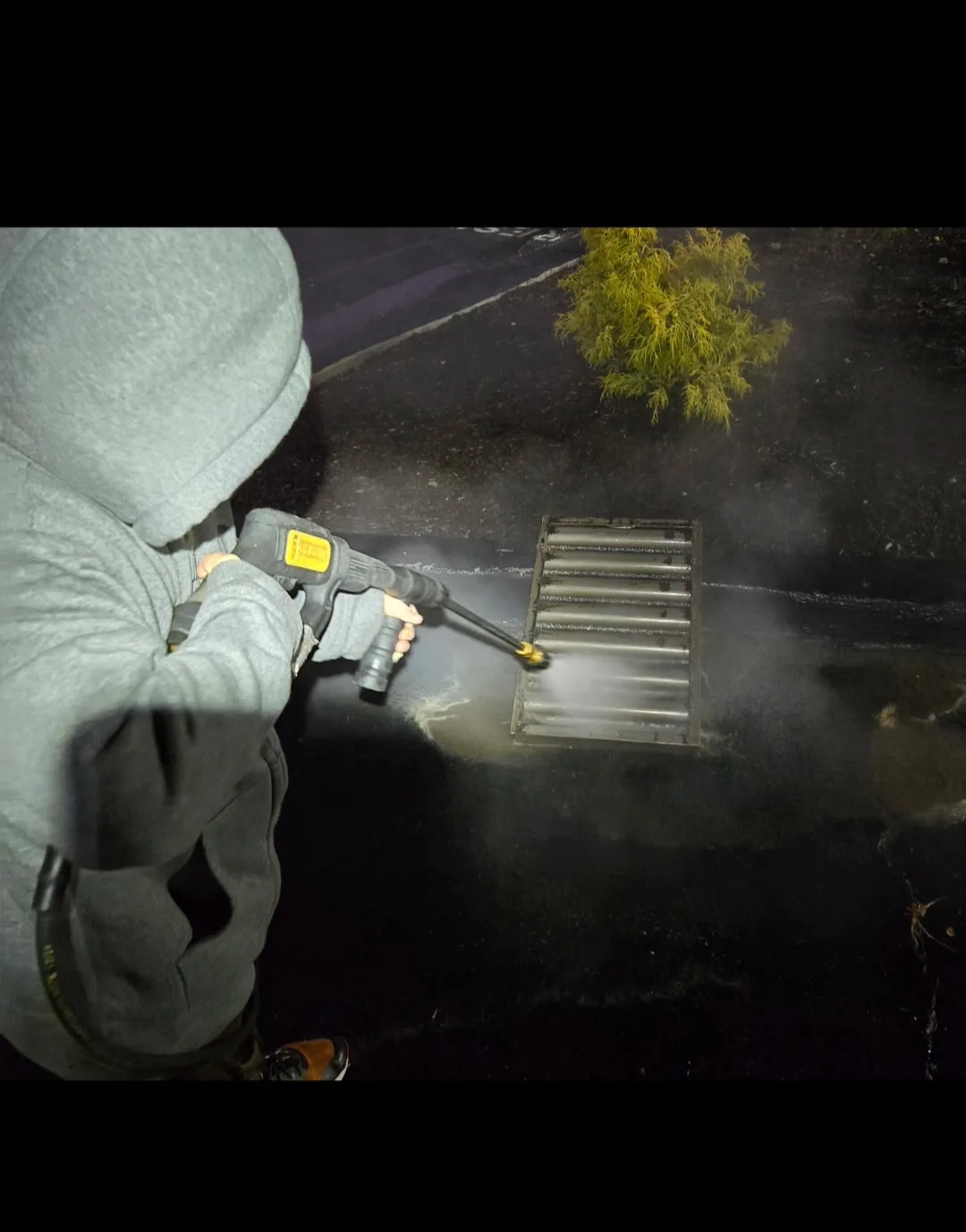 Tyler's son pressure washing a grease filter on a commercial kitchen rooftop at night